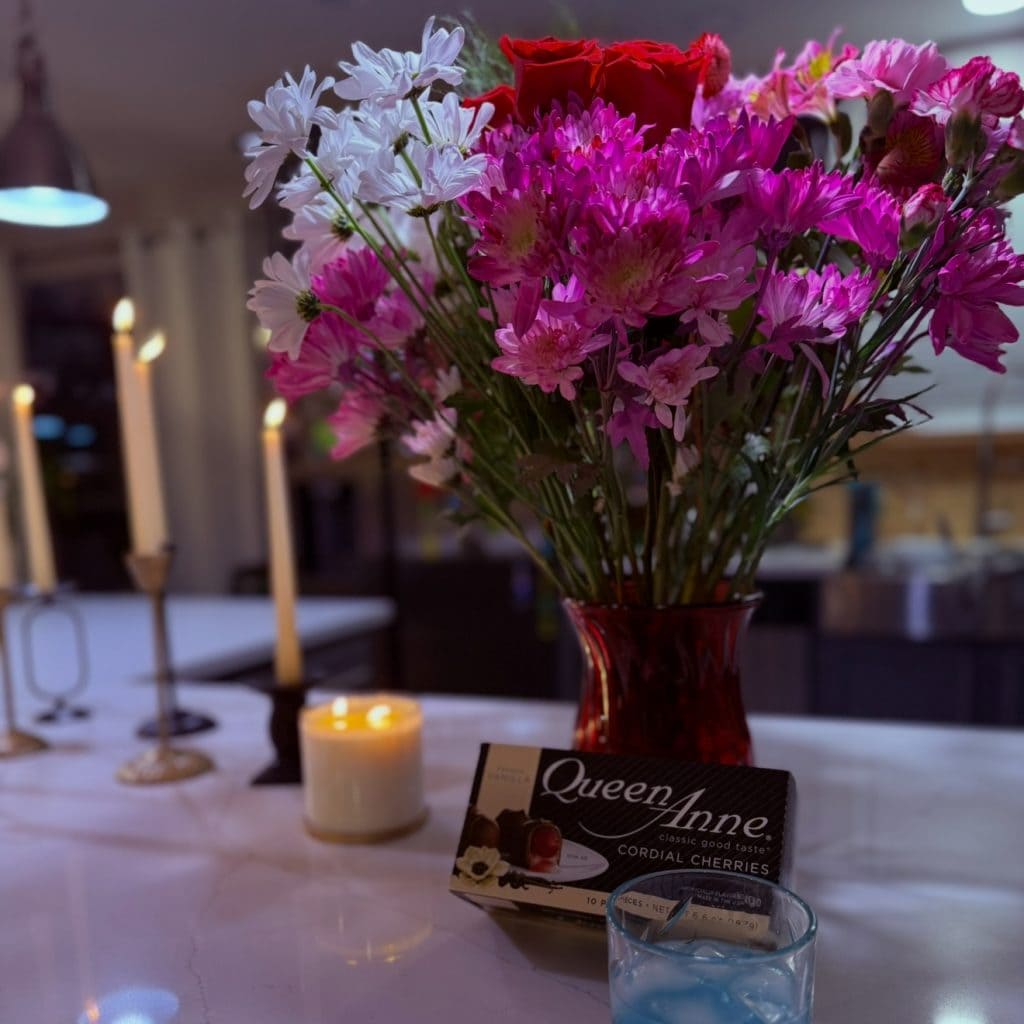 Vase of pink and red flowers with candles and chocolates on a table, symbolizing love, memory, and joy after grief