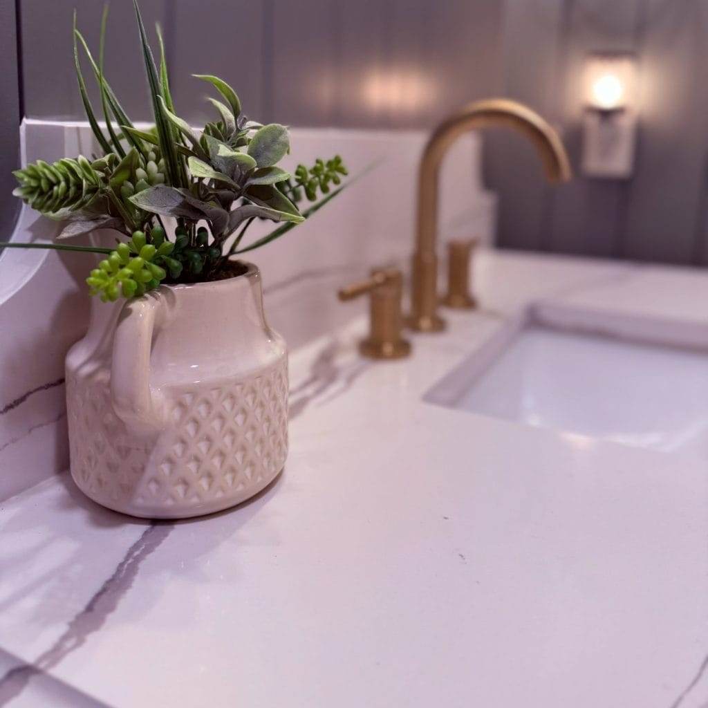 Bathroom vanity with quartz countertop, gold faucet, and decorative vase with greenery, styled in a cozy modern home.
